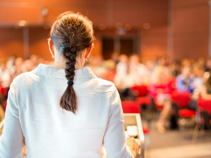 Kvindelig oplægsholder med fletning foran forsamling af uddannelsesansvarlige